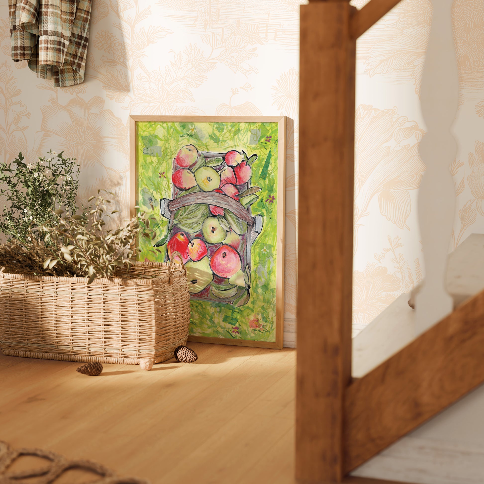 Framed artwork of apples on a wall next to a woven basket with plants