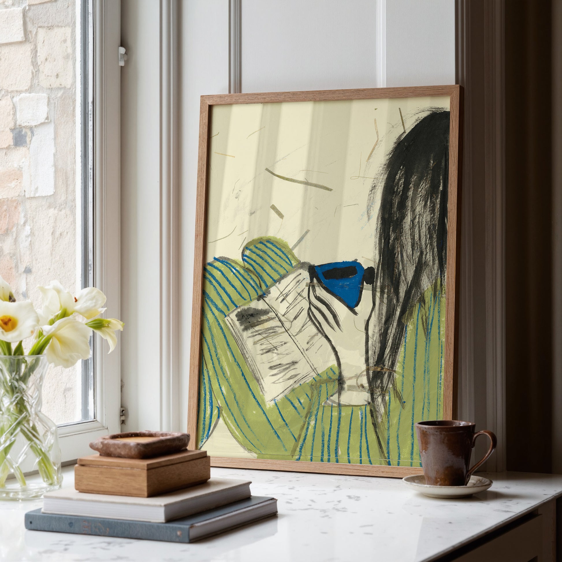 Framed Illustration of a girl wearing a striped pyjama, reading a book and drinking out of a blue mug.
