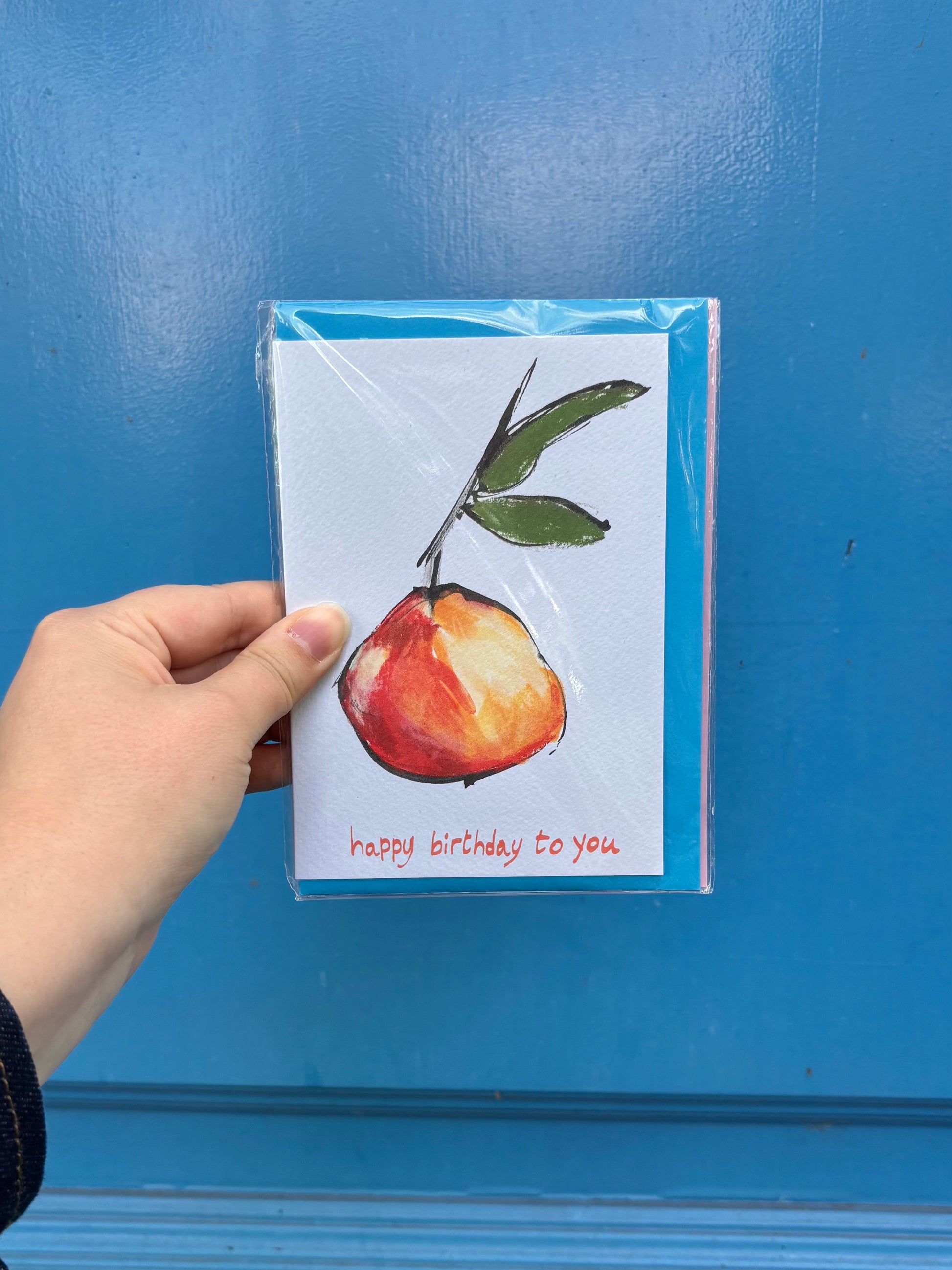 Hand holding a card with a pear illustration and 'happy birthday to you' text against a blue background