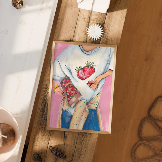 Framed artwork of a person wearing a sweater with strawberry designs on a wooden surface.