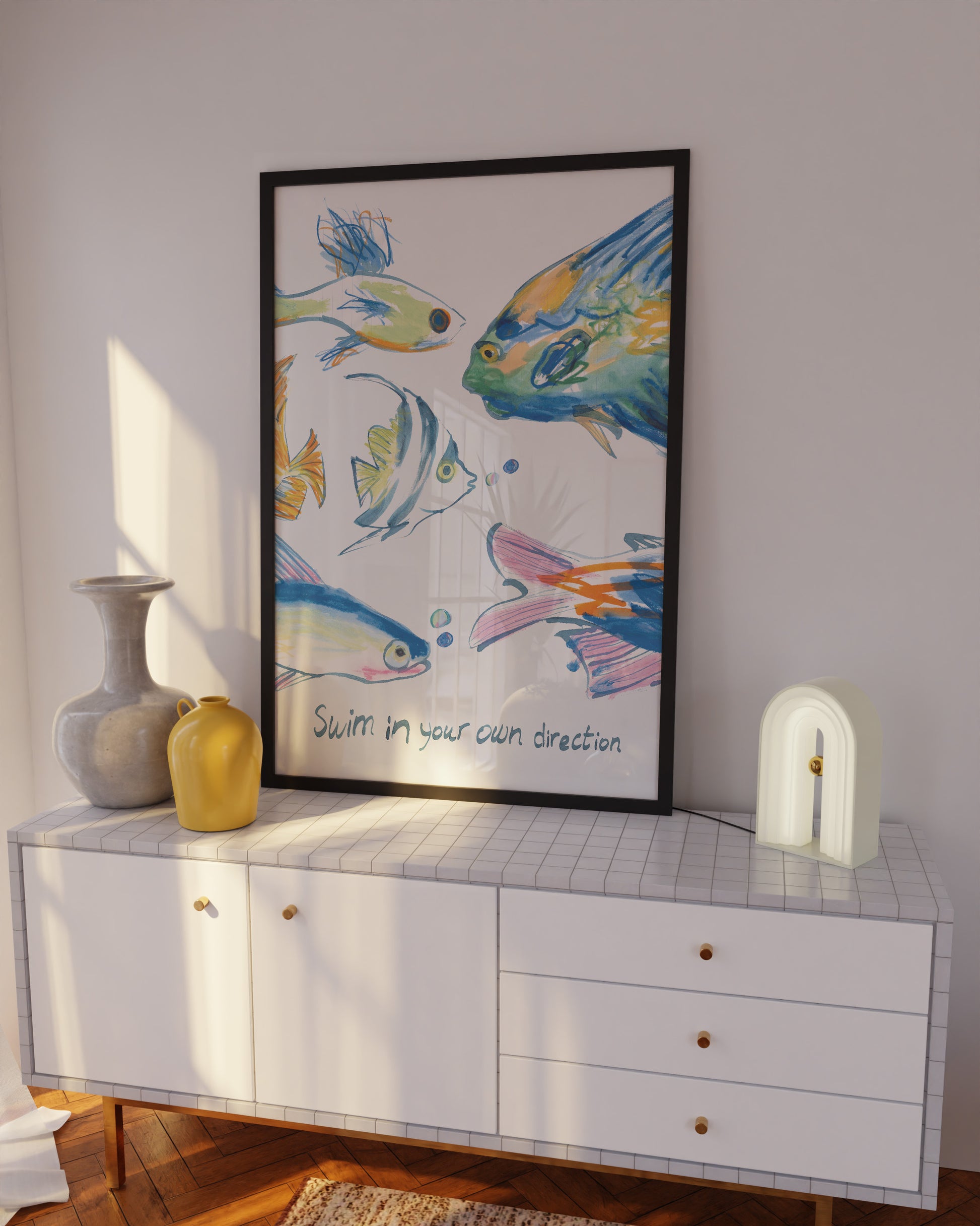 Framed artwork of colorful fish on a wall above a white cabinet.