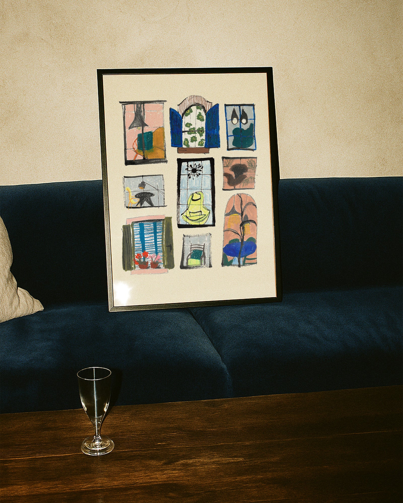 Framed artwork on a wall above a couch with a glass on a table in the foreground.