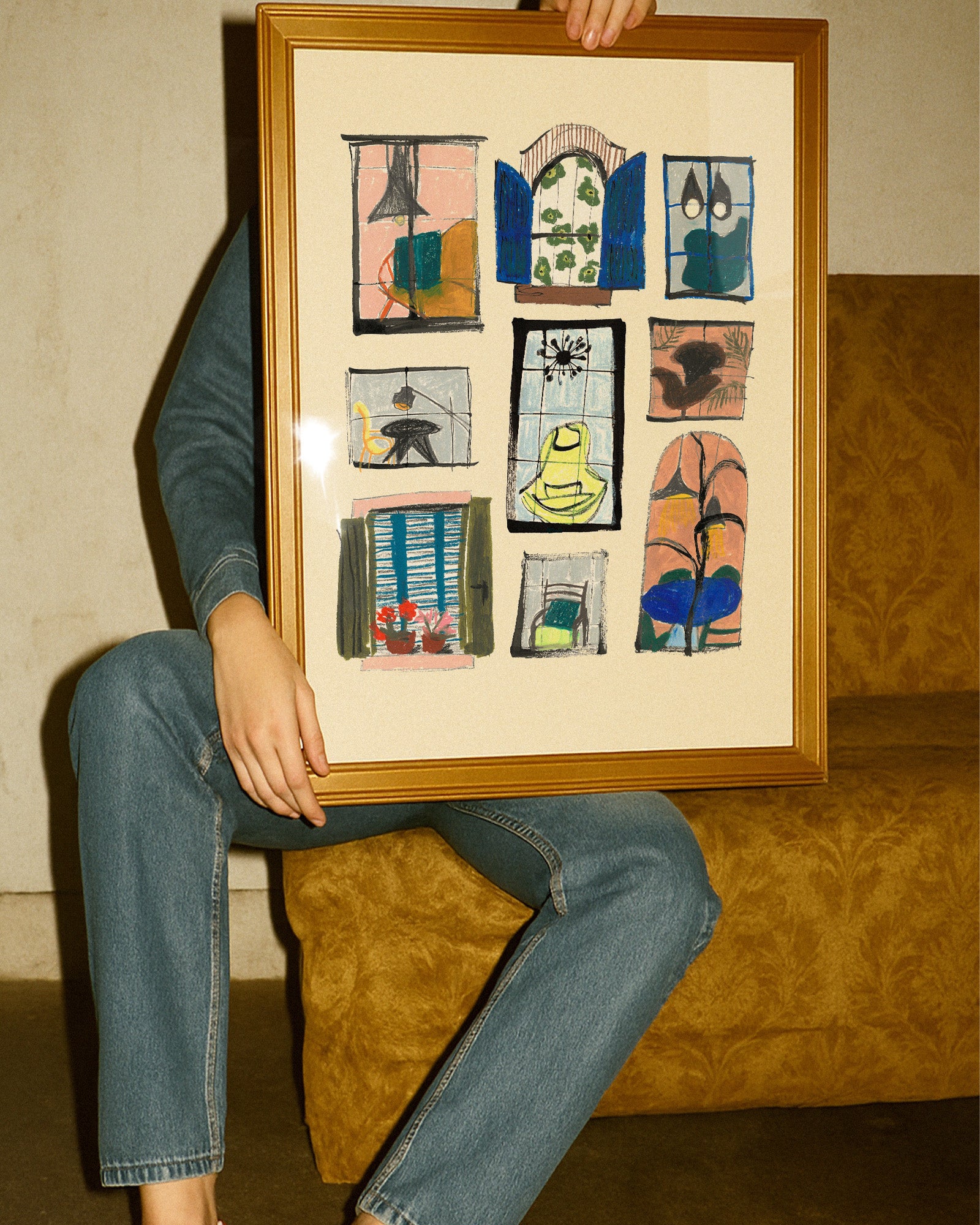 Person holding a framed collage of small artworks against a textured wall.