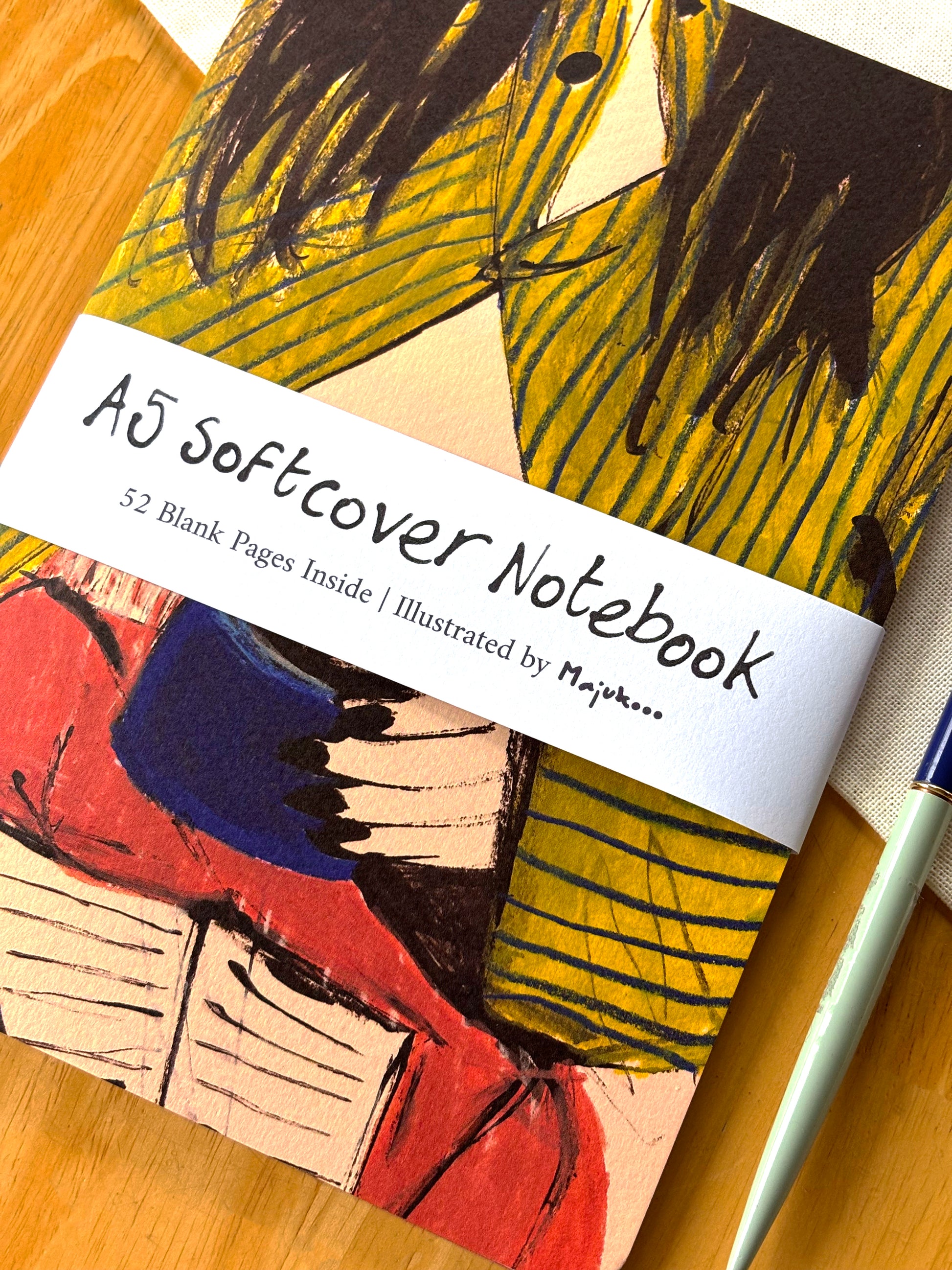 A5 softcover notebook with colorful illustration and 'Majukooo' branding on a wooden surface.