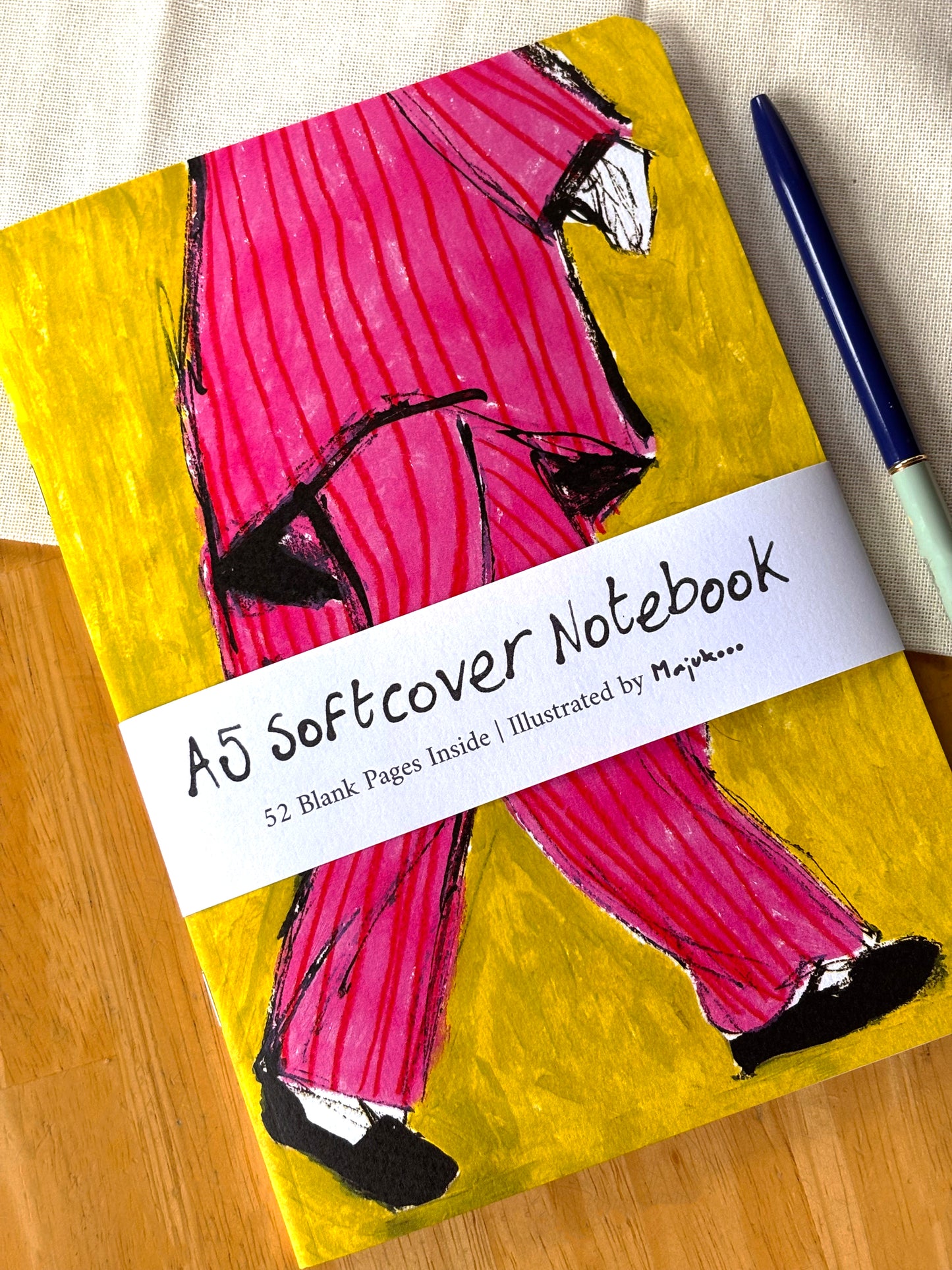 Notebook with a colorful cover featuring a person in pink pants on a wooden surface.