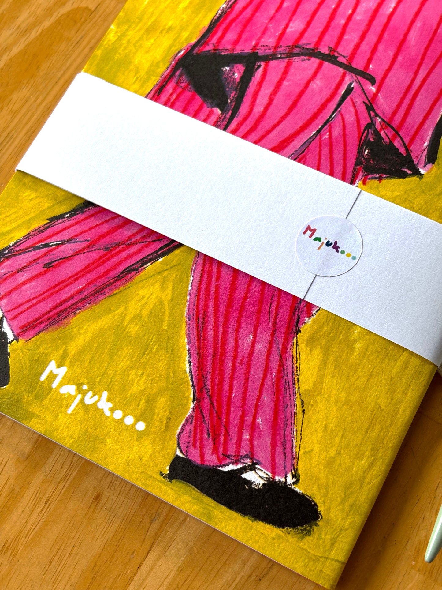 Artistic depiction of a person in pink pants on a yellow background with 'Majukooo' branding.