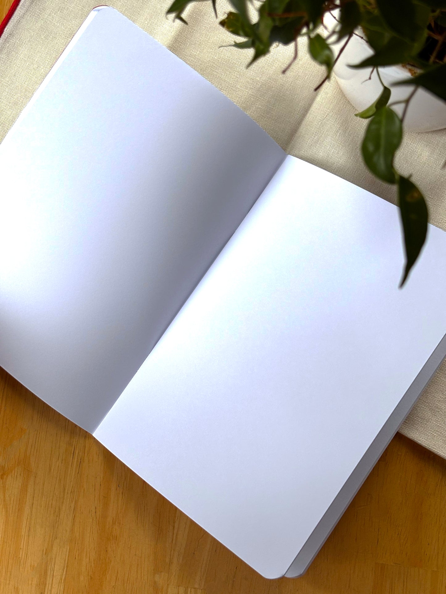 Open notebook with blank pages on a wooden surface with a plant in the background