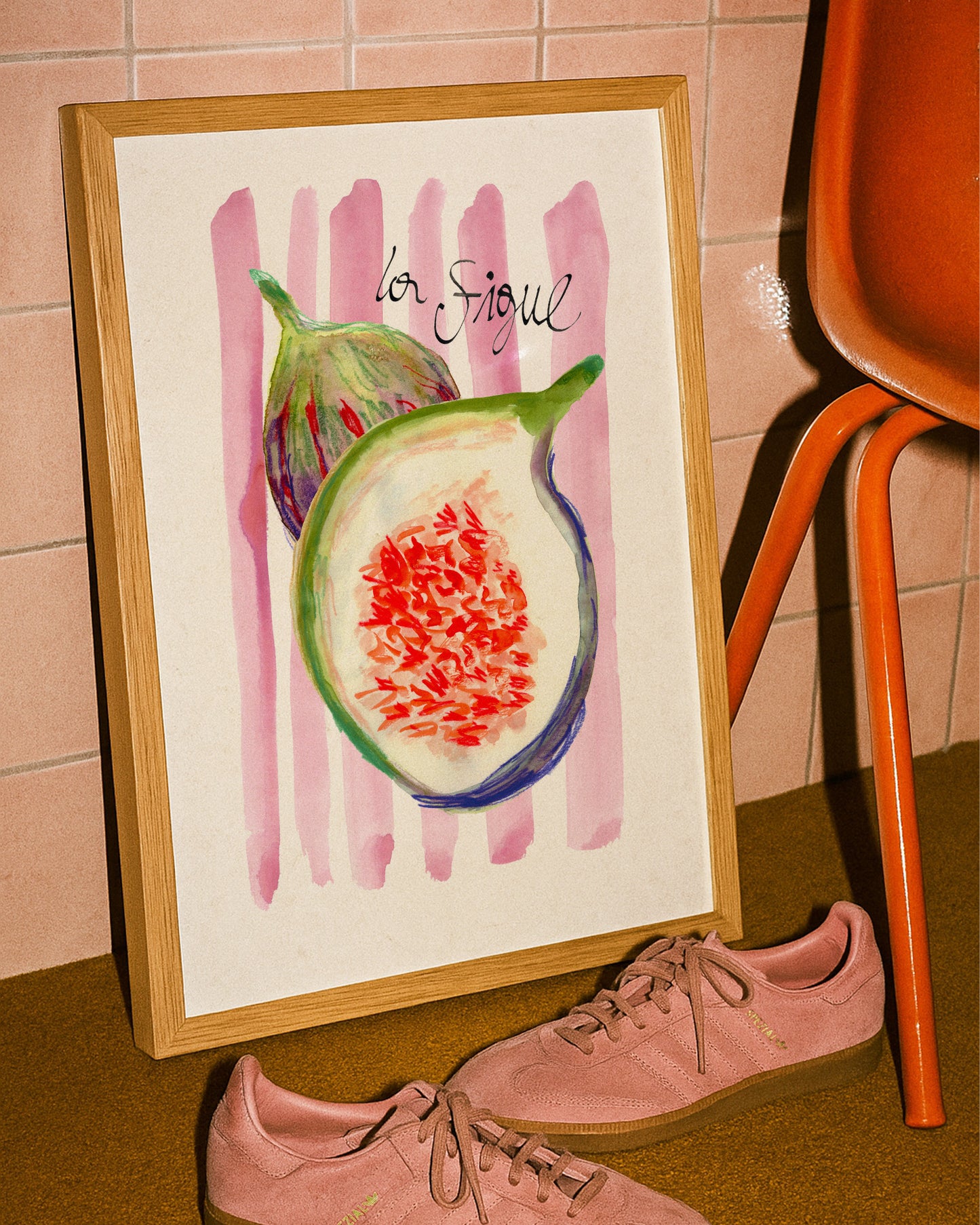 Framed artwork of a fig with 'la Figue' text on a pink background, next to pink sneakers and an orange chair.